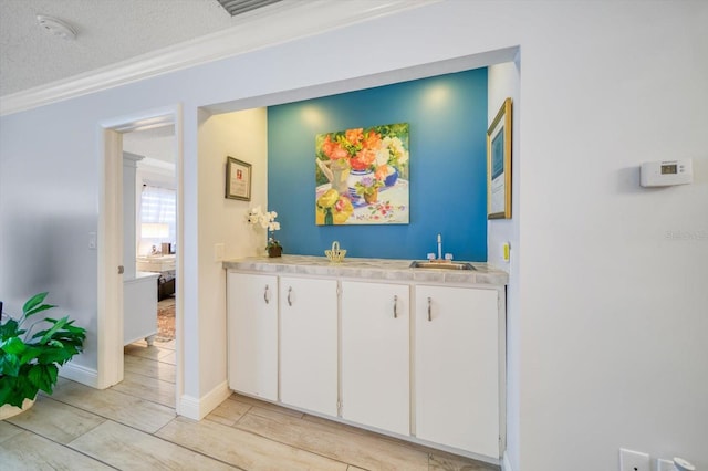 interior space featuring sink, light tile floors, ornamental molding, a textured ceiling, and white cabinetry