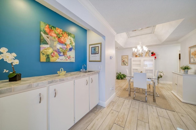 kitchen with an inviting chandelier, white cabinetry, crown molding, light hardwood / wood-style flooring, and a raised ceiling