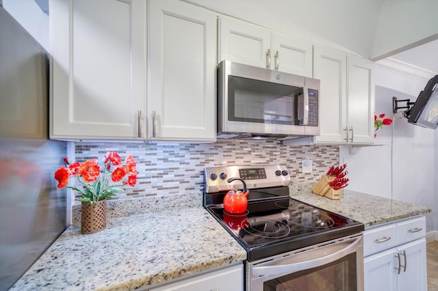 kitchen with light stone countertops, tasteful backsplash, stainless steel appliances, and white cabinetry