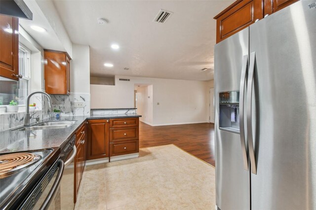 kitchen featuring backsplash, dark stone counters, sink, light hardwood / wood-style flooring, and appliances with stainless steel finishes