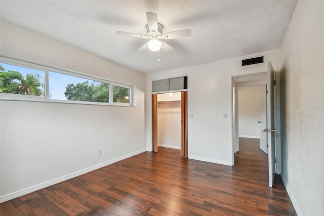 unfurnished bedroom with a walk in closet, ceiling fan, a closet, and dark wood-type flooring