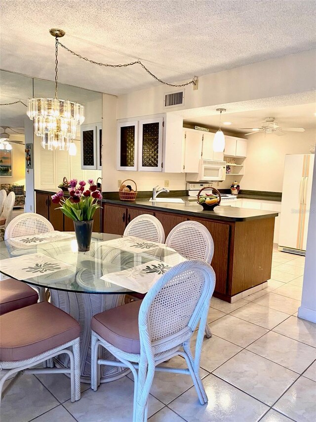 dining area with a textured ceiling, light tile patterned floors, ceiling fan with notable chandelier, and visible vents