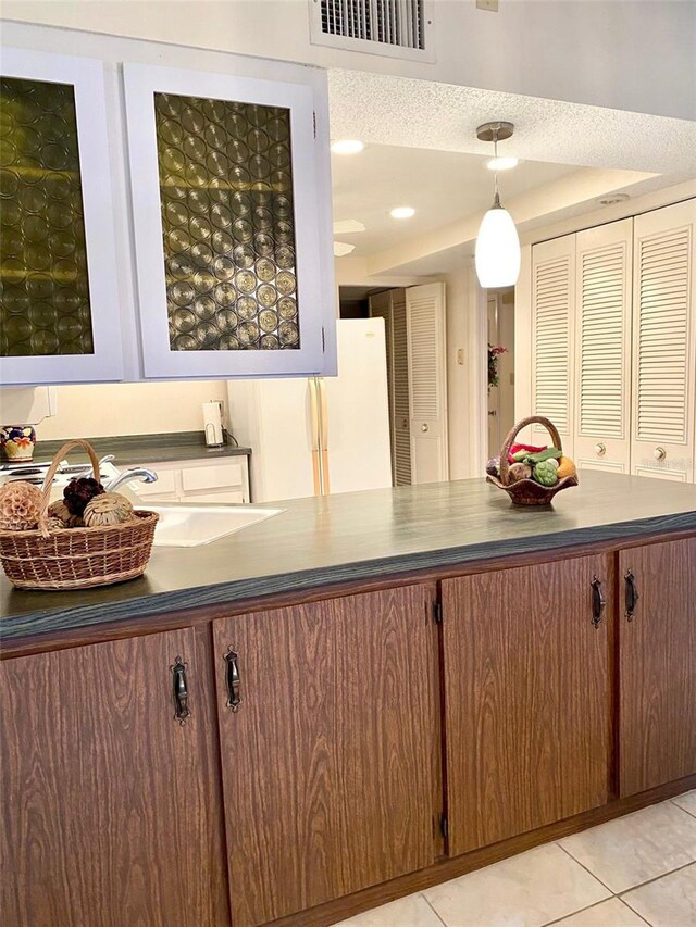 kitchen with light tile patterned floors, dark countertops, visible vents, hanging light fixtures, and freestanding refrigerator