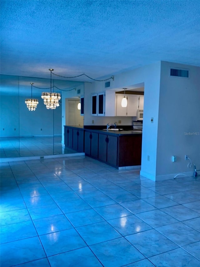 kitchen with a textured ceiling, light tile patterned floors, dark countertops, and visible vents