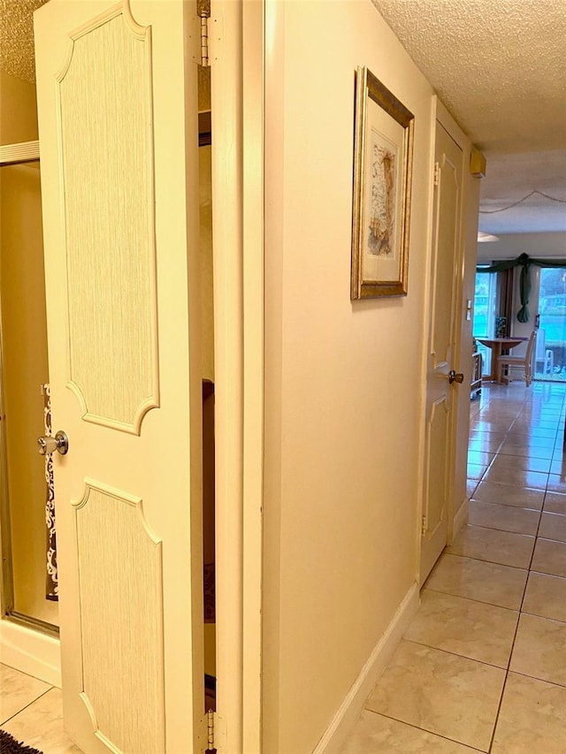 corridor with a textured ceiling, baseboards, and light tile patterned floors