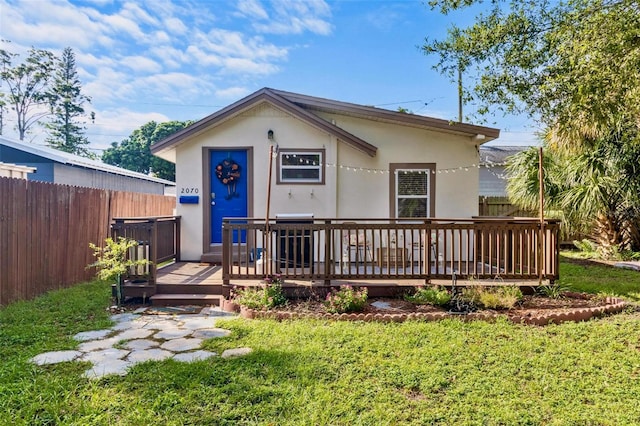 view of front of property with a front yard, fence, a deck, and stucco siding