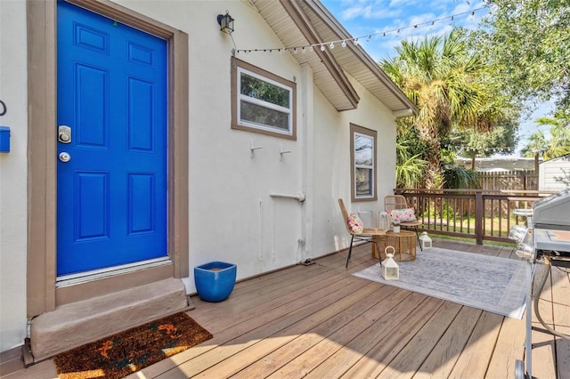 entrance to property with fence, a wooden deck, and stucco siding