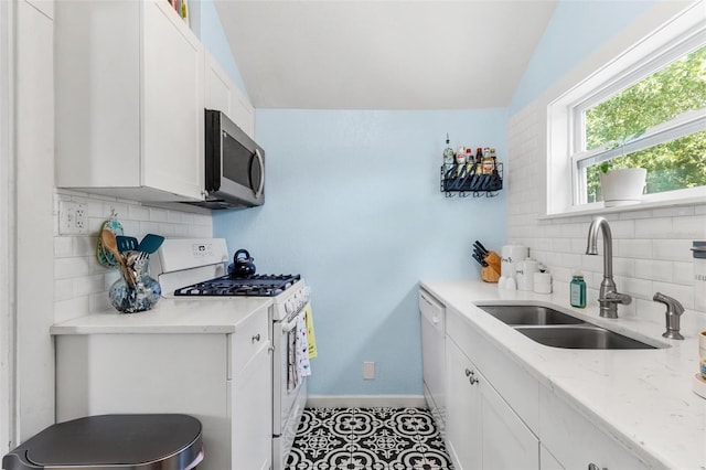 kitchen featuring white appliances, a sink, white cabinetry, baseboards, and light stone countertops