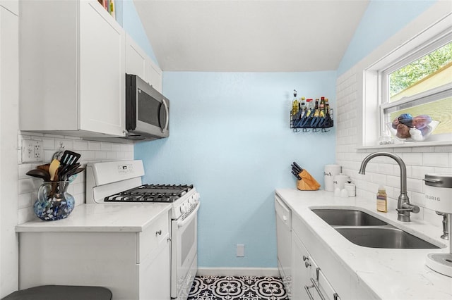 kitchen with white appliances, baseboards, white cabinets, light stone counters, and a sink