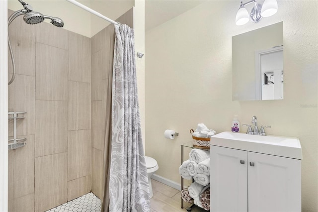 bathroom with baseboards, a tile shower, vanity, and toilet