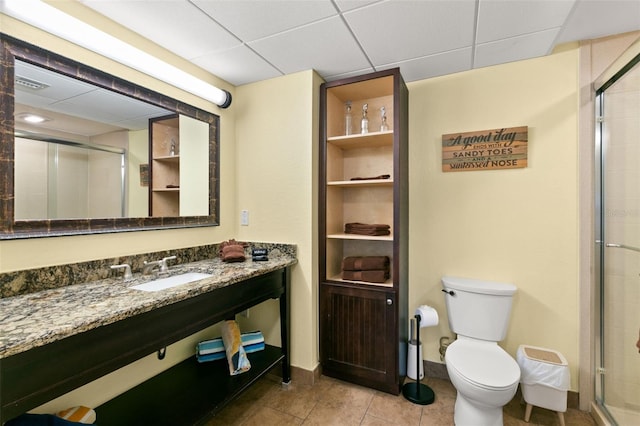 bathroom featuring vanity, a drop ceiling, a shower with door, tile patterned floors, and toilet