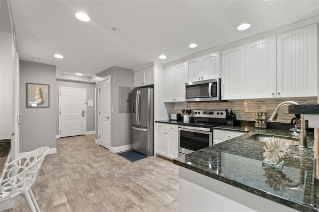 kitchen with white cabinets, appliances with stainless steel finishes, dark stone countertops, light wood-style floors, and a sink