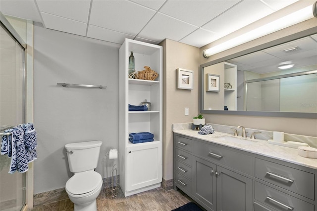 bathroom with a drop ceiling, vanity, hardwood / wood-style flooring, toilet, and a shower with shower door