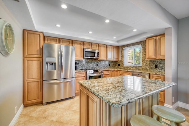 kitchen featuring backsplash, light stone countertops, appliances with stainless steel finishes, a kitchen island, and a kitchen bar