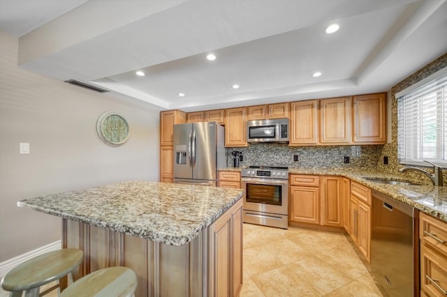 kitchen featuring a kitchen breakfast bar, a raised ceiling, light stone counters, backsplash, and appliances with stainless steel finishes