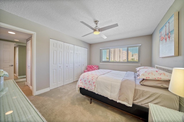 bedroom featuring ceiling fan, a closet, light colored carpet, and a textured ceiling