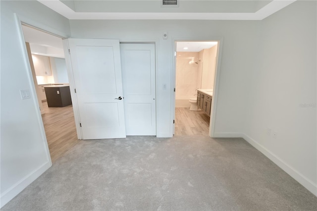 unfurnished bedroom with ensuite bathroom, a closet, and light colored carpet