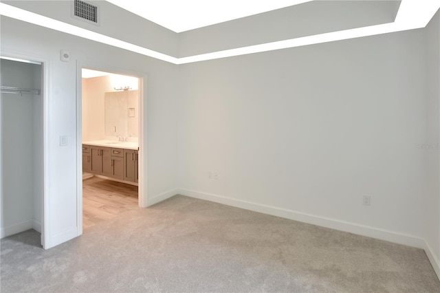 unfurnished bedroom featuring ensuite bathroom, light colored carpet, and a closet