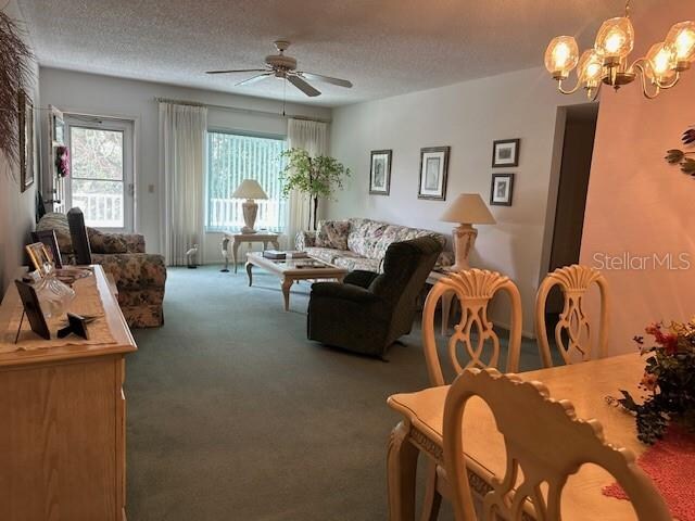 living room featuring a textured ceiling, ceiling fan with notable chandelier, and carpet floors