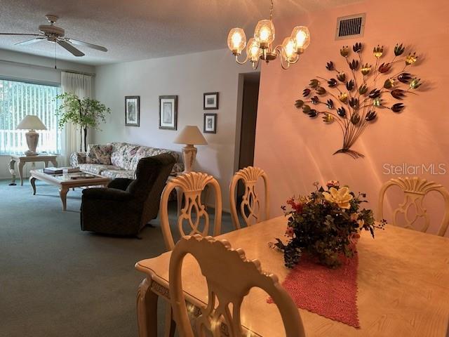 dining space with carpet floors, a textured ceiling, and ceiling fan with notable chandelier