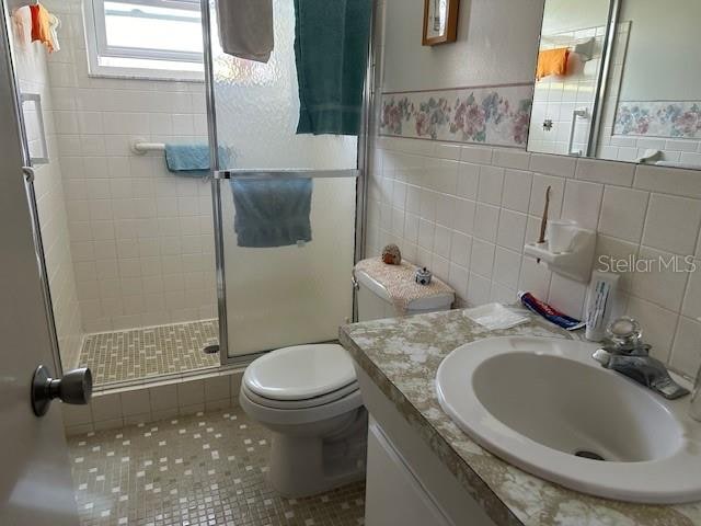 bathroom featuring tile walls, a shower with door, tasteful backsplash, toilet, and oversized vanity