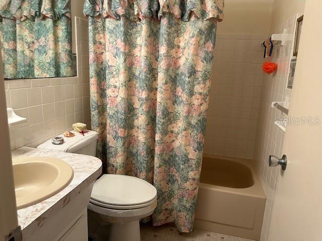 full bathroom with tile walls, toilet, vanity, and shower / tub combo with curtain