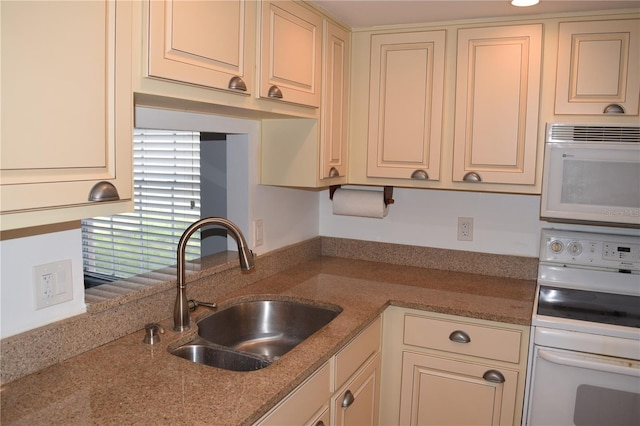 kitchen with light stone countertops, white appliances, sink, and cream cabinetry