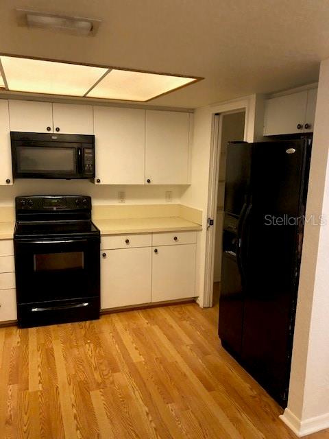 kitchen with black appliances, white cabinets, and light wood-type flooring