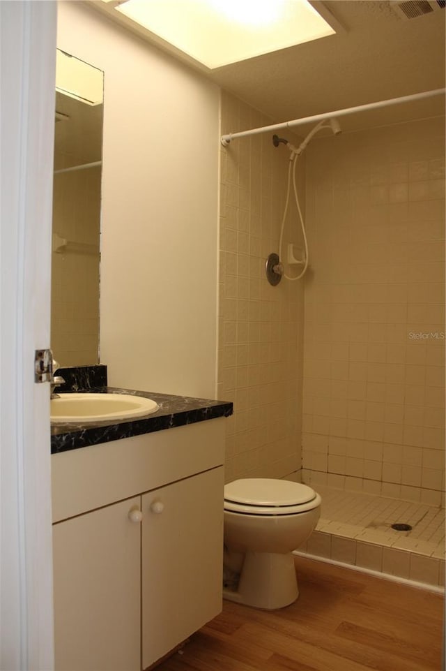 bathroom with wood-type flooring, vanity, a tile shower, and toilet