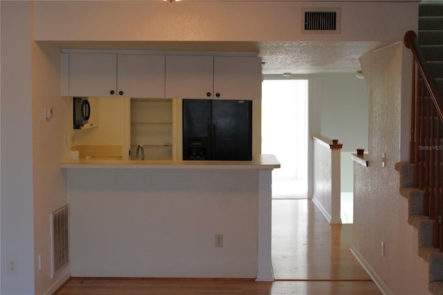 kitchen featuring black appliances, kitchen peninsula, a textured ceiling, and light hardwood / wood-style flooring