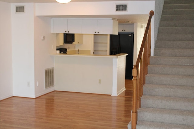 kitchen with white cabinets, wood-type flooring, kitchen peninsula, and black appliances