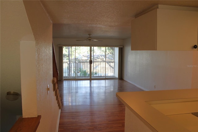 living room with a textured ceiling, ceiling fan, and dark wood-type flooring