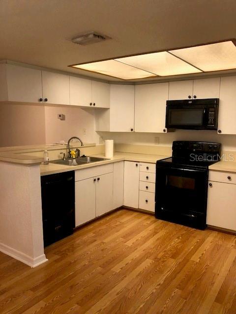 kitchen with black appliances, light wood-type flooring, white cabinetry, and sink