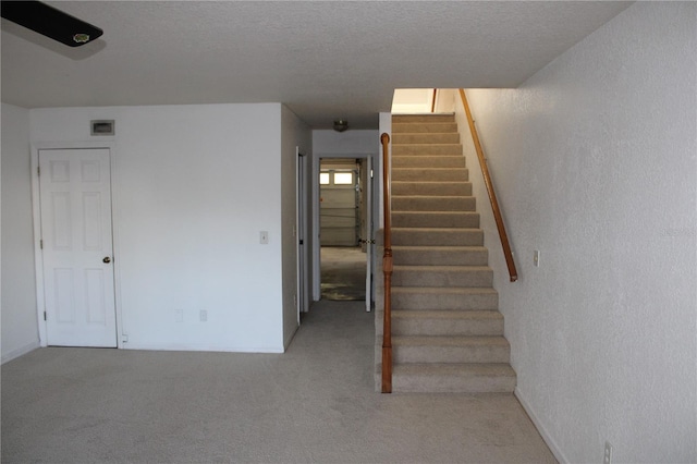 stairway featuring a textured ceiling and carpet floors