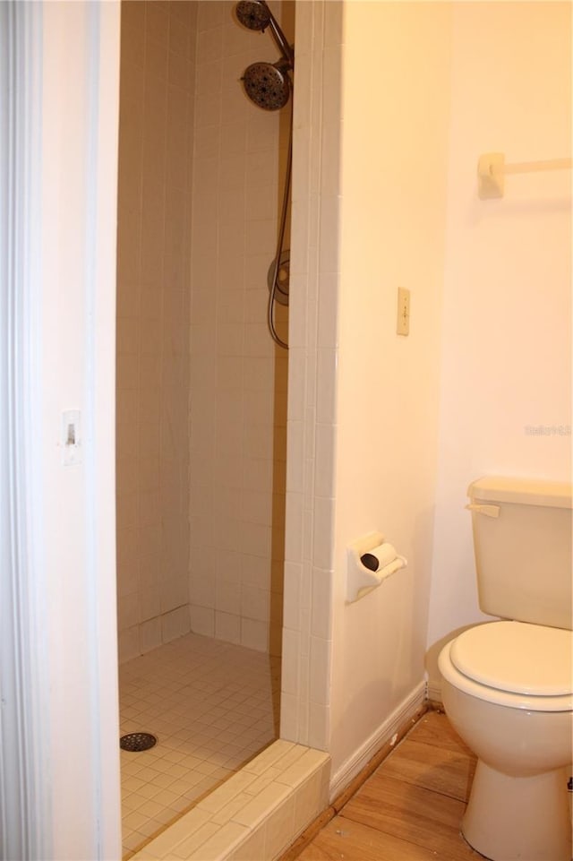 bathroom with a tile shower, toilet, and hardwood / wood-style floors