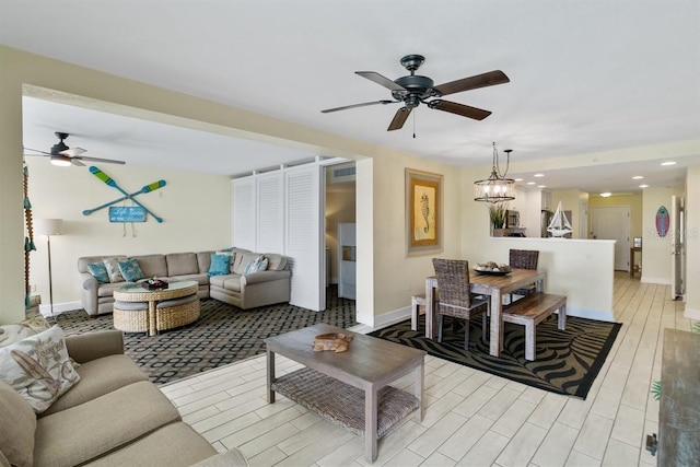 living room featuring ceiling fan with notable chandelier and light wood-type flooring