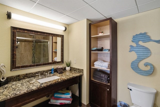 bathroom with a drop ceiling, an enclosed shower, vanity, and toilet