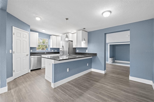 kitchen featuring kitchen peninsula, appliances with stainless steel finishes, hardwood / wood-style flooring, white cabinetry, and hanging light fixtures