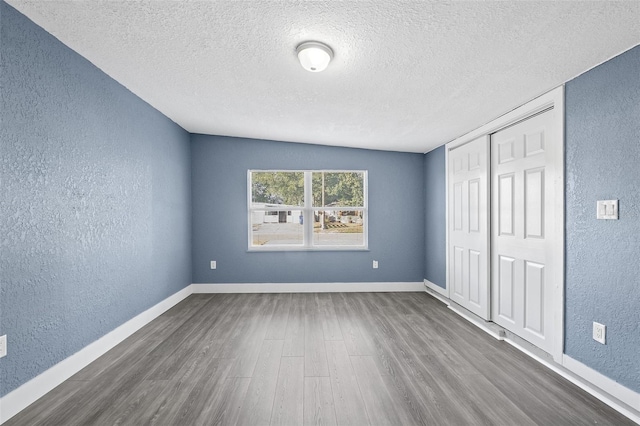 unfurnished bedroom with a closet, dark hardwood / wood-style flooring, a textured ceiling, and vaulted ceiling