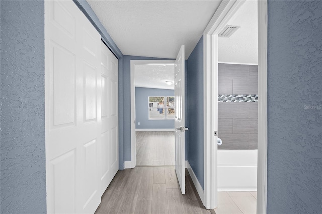 hallway featuring a textured ceiling, light hardwood / wood-style flooring, and lofted ceiling