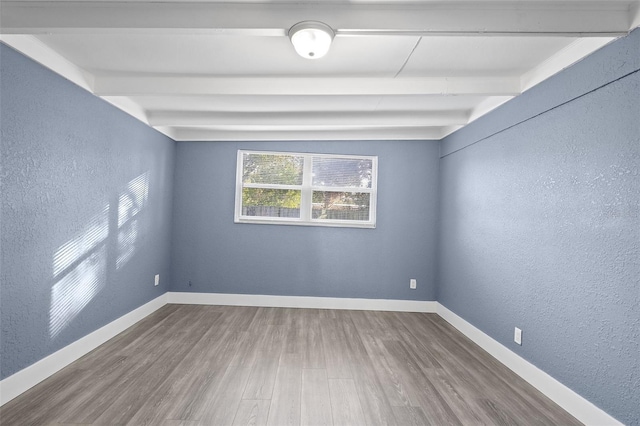 spare room featuring beamed ceiling and hardwood / wood-style flooring