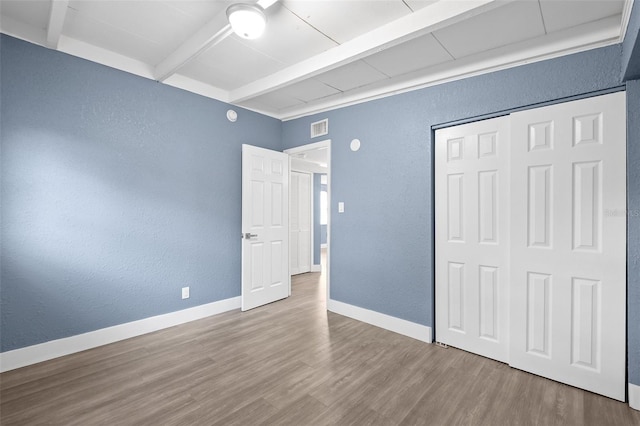 unfurnished bedroom featuring hardwood / wood-style floors, a closet, and beam ceiling