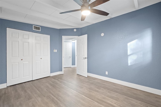 unfurnished bedroom with beam ceiling, light wood-type flooring, a closet, and ceiling fan