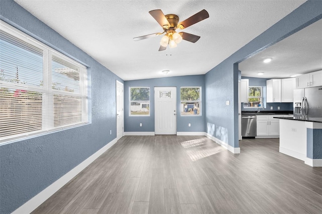 unfurnished living room with dark wood-type flooring, vaulted ceiling, ceiling fan, and a healthy amount of sunlight