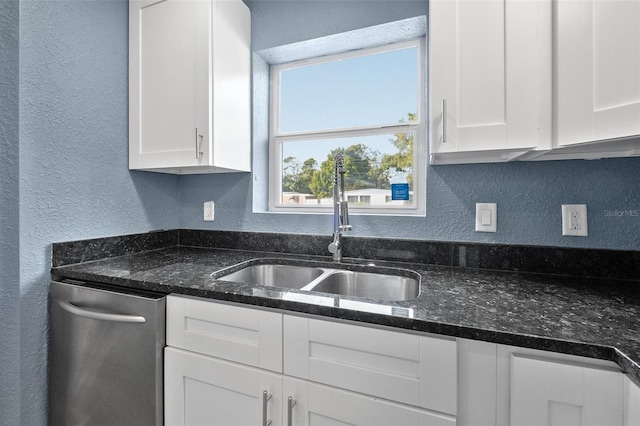 kitchen with dark stone countertops, white cabinetry, sink, and stainless steel dishwasher