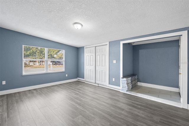 unfurnished bedroom with a textured ceiling, dark hardwood / wood-style floors, and lofted ceiling