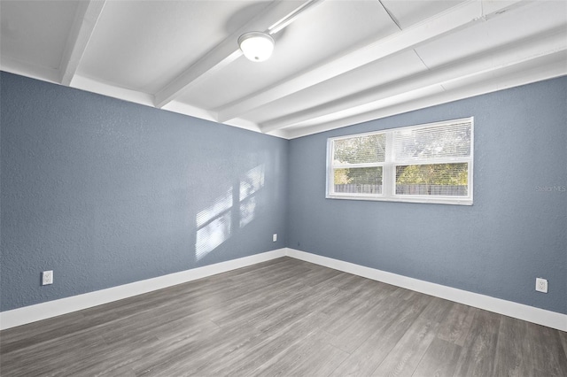 empty room featuring beamed ceiling and dark wood-type flooring