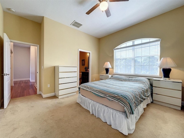 carpeted bedroom with ensuite bath, baseboards, visible vents, and ceiling fan