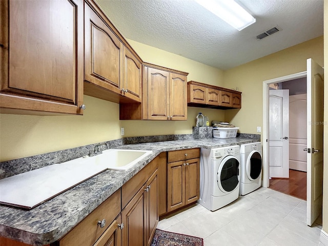 laundry area featuring visible vents, cabinet space, a sink, a textured ceiling, and washing machine and dryer