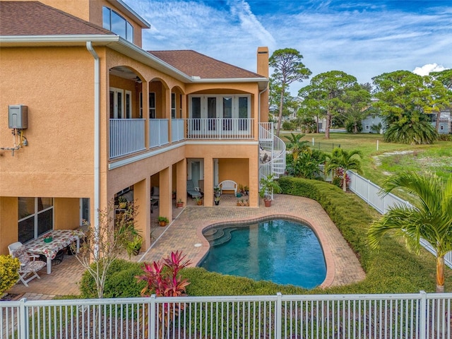 rear view of property with stucco siding, a fenced backyard, a balcony, a chimney, and a patio area